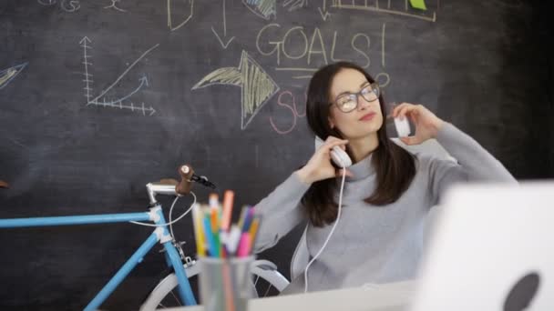4K Entrepreneur businesswoman putting on headphones and relaxing at her desk - Imágenes, Vídeo