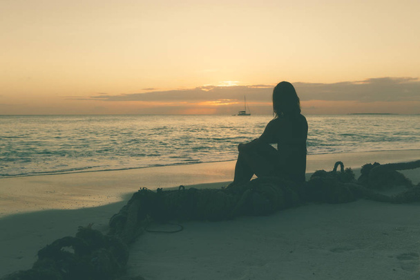 Mujer joven sentada en la playa y disfrutando del atardecer
  - Foto, imagen