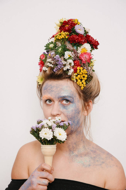 Egy fiatal nő, virágokkal a fejét és a kezét. Tavaszi kép virágokkal. A lány és a virágzó haircut és brokát arcán. - Fotó, kép