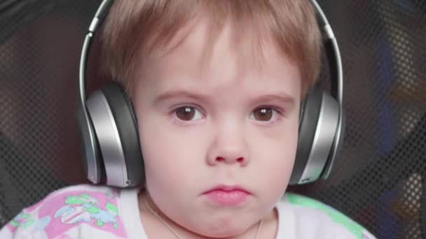 un niño pequeño se sienta en una silla y escucha música a través de auriculares. Cara de cerca
 - Imágenes, Vídeo