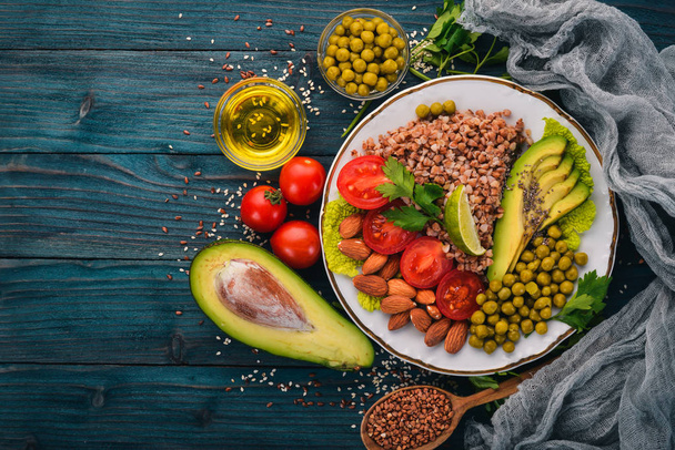 Healthy food. Buckwheat, cherry tomatoes, avocados, almonds and green peas. On a wooden background. Top view. Free space for your text. - Fotó, kép
