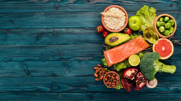 Healthy food. Fish salmon, avocado, broccoli, fresh vegetables, nuts and fruits. On a wooden background. Top view. Copy space. - Φωτογραφία, εικόνα