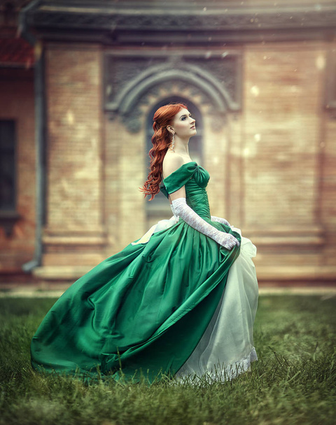 Beautiful, young, red-haired girl in a green medieval dress, climbs the stairs to the castle. - Fotó, kép