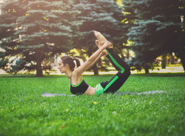 Vrouw opleiding yoga in boog pose buitenshuis - Foto, afbeelding