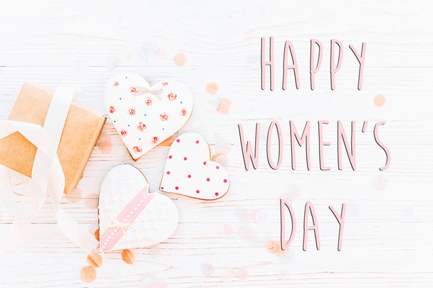 happy women's day text sign flat lay. 8 march. pink hearts and present and confetti on white rustic wooden background. space for text. greeting card concept. womens bright image - Fotó, kép