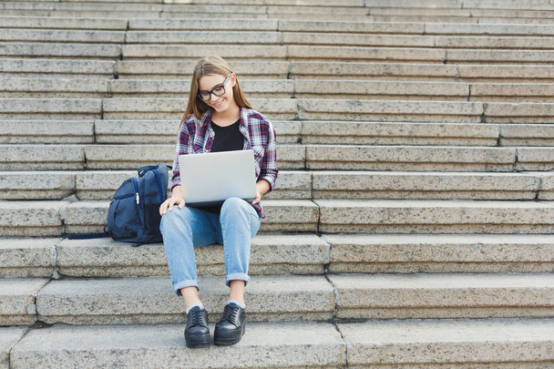 Smiling student sitting on stairs using laptop - Fotó, kép
