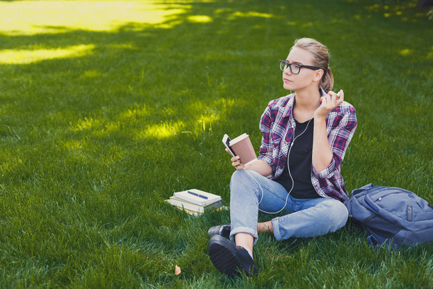 Jonge vrouw, luisteren naar muziek op gras buitenshuis - Foto, afbeelding