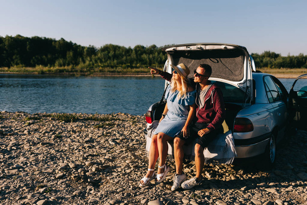 Couple voyageur heureux debout près du coffre ouvert de la voiture et regarder le lever du soleil
 - Photo, image