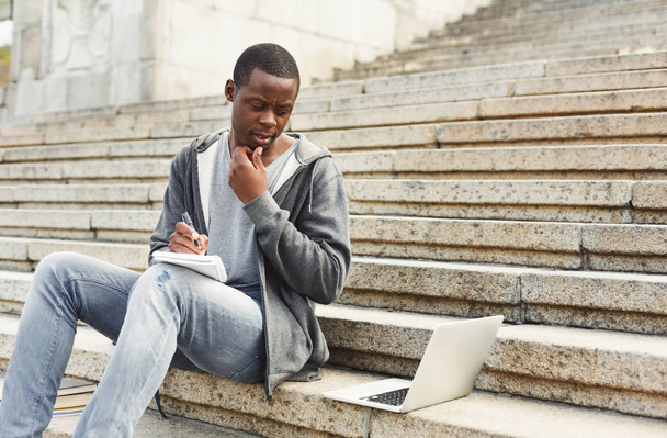 Estudante afro-americano concentrado estudando com laptop e notebook ao ar livre
 - Foto, Imagem