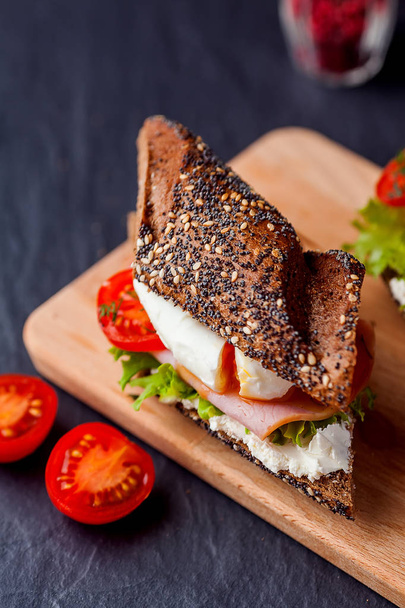 Sandwich with ham, poached egg and fresh tomatoes on wooden boar - Foto, Imagem