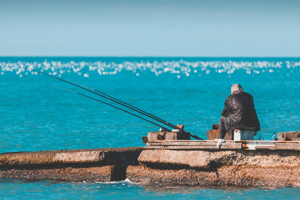 An elderly lonely man is fishing on a sea pier. - Photo, Image