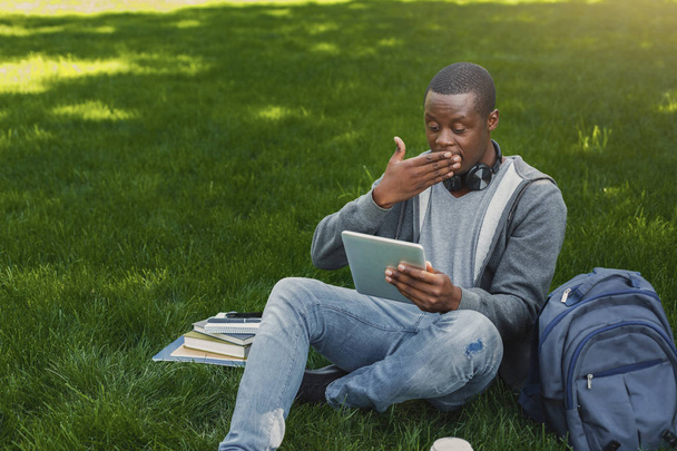 Surprised african-american student on grass with tablet oudoors - 写真・画像