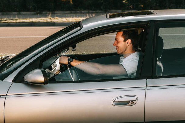 Jeune homme caucasien attrayant en t-shirt blanc assis dans la voiture
 - Photo, image