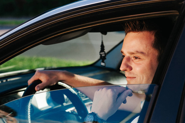 Jovem atraente caucasiano homem em branco t-shirt sentado no carro
 - Foto, Imagem