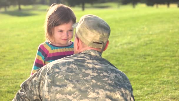 Στρατιώτης σε camoubackgrounde που αγκαλιάζει την κόρη του στο πάρκο. - Πλάνα, βίντεο