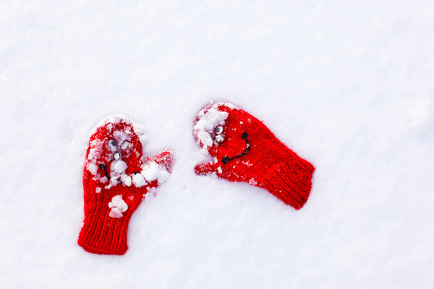 rode gebreide wanten met ogen op zachte pluizige sneeuw - Foto, afbeelding