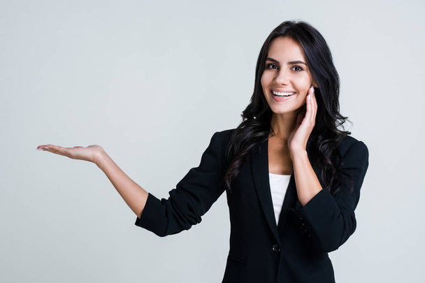 Have you seen this? Beautiful young businesswoman pointing away and looking at camera with smile while standing against white background - Photo, Image