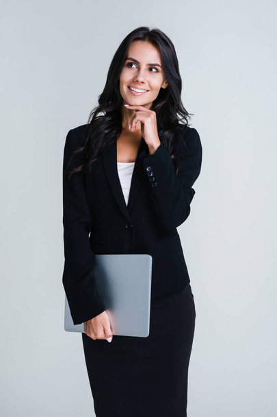 In love with her job. Beautiful young businesswoman holding her laptop and looking pensive while standing against white background - Photo, Image