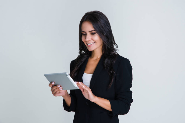 Tecnología en su vida. Hermosa joven empresaria usando su tableta digital con sonrisa mientras está de pie sobre fondo blanco
 - Foto, imagen