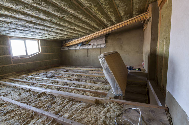 De zolder van het huis in aanbouw. Mansard muren en plafond-isolatie met steenwol. Glasvezel isolatiemateriaal in houten frame voor koude barrière - Foto, afbeelding