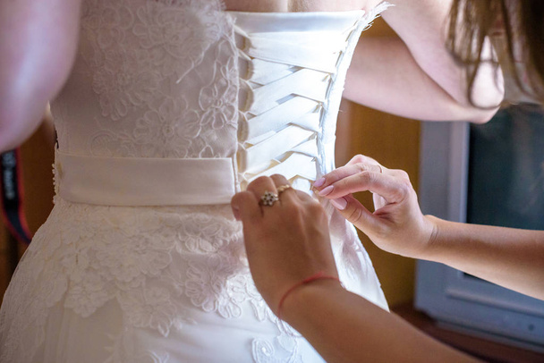 Руки крупным планом шнуруют корсет свадебного платья
 - Фото, изображение