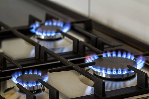 Erdgas, das im Dunkeln auf einem Küchengasherd brennt. Panel aus Stahl mit einem Gasringbrenner auf schwarzem Hintergrund, Nahaufnahme - Foto, Bild