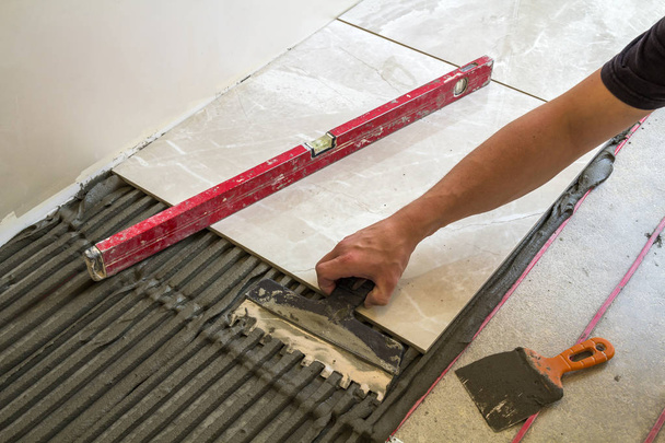 Keramische tegels en hulpmiddelen voor de tegelzetter. Werknemer hand vloertegels installeren. Verbetering van het huis, renovatie - keramische tegel vloer lijm, mortel, niveau. - Foto, afbeelding
