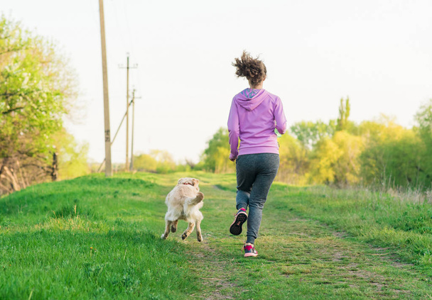 Joven chica bonita corriendo al aire libre en la primavera con el perro
 - Foto, Imagen
