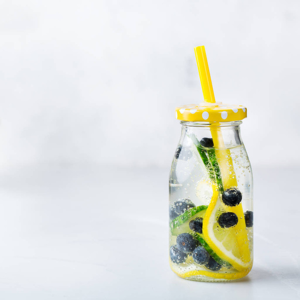 Health care, fitness, healthy nutrition diet concept. Fresh cool lemon cucumber berry infused water, cocktail, detox drink, lemonade in a glass bottle for spring summer days. Copy space background - 写真・画像