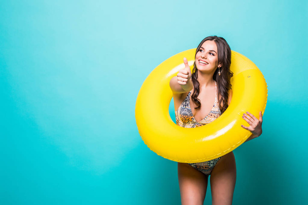 Beauty young woman in swimsuit with an inflatable ring and hand showing thumbs up gesture isolated over green background - Photo, Image