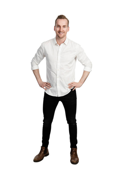 Handsome man standing in front of a white background wearing a white shirt and black jeans looking at camera. - Foto, Bild