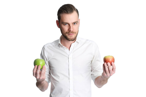 Focused man in a white shirt holding two apples, one green and one red, looking at camera. White background. - Foto, afbeelding