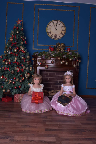 two sisters in white with pink dress sitting with gifts in hands in christmas - Фото, зображення