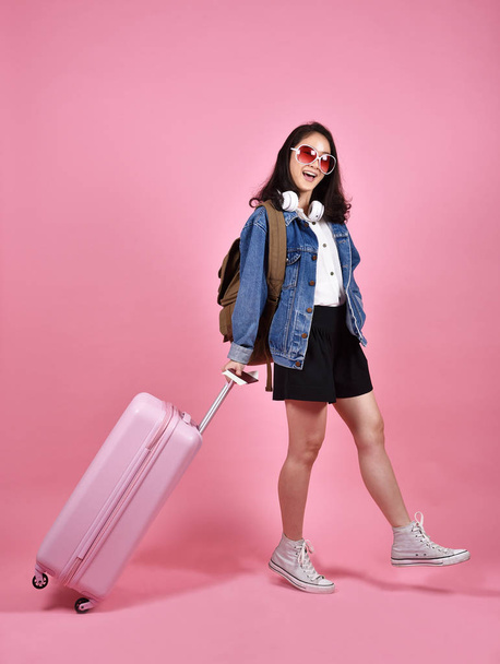 Vacanza e concetto di viaggio, viaggiatore donna sorridente in possesso di valigia rosa e passaporto documento su sfondo rosa
. - Foto, immagini
