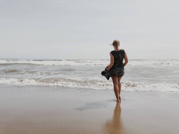Mädchen in einem sich im Wind entwickelnden Kleid auf dem Hintergrund des Ozeans. - Foto, Bild