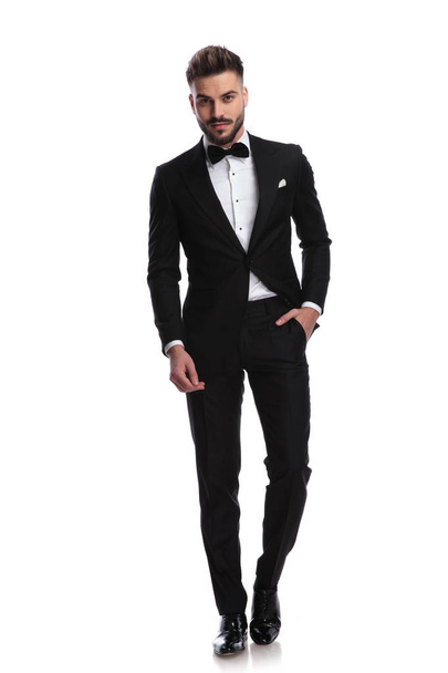 smiling man in tuxedo stands with one hand in pocket - Фото, изображение