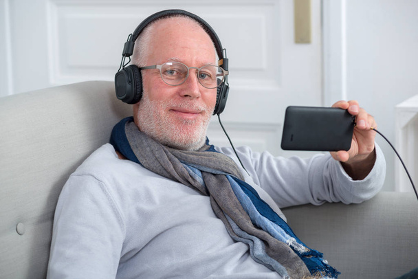 Senior man in headphones listening to music at home
 - Фото, изображение