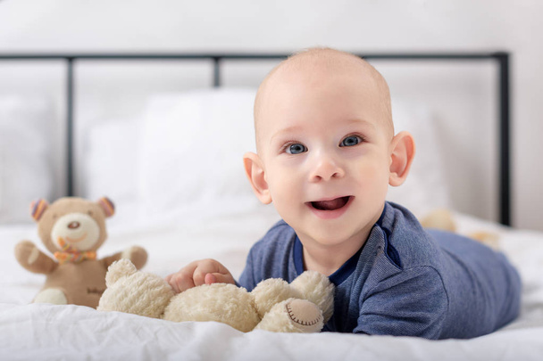 Adorable baby boy laughing and playing with toy bears on a bed. Newborn child relaxing in bed. Family morning at home. - Photo, image