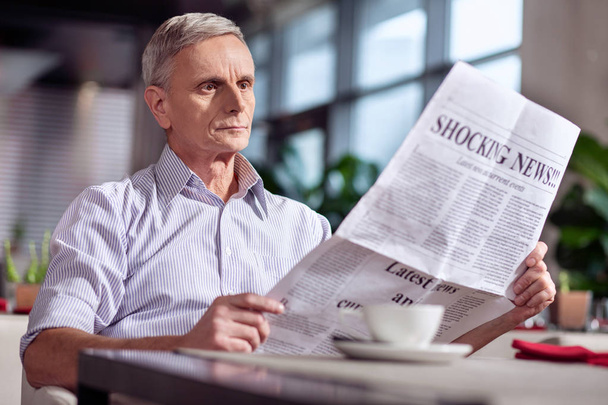 Astonished mature man looking through newspaper - Фото, зображення