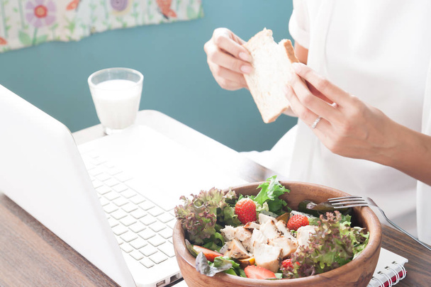 Femme au travail avec repas du matin, accent sélectif sur la salade et la femme tenant du pain tranché en arrière-plan
 - Photo, image