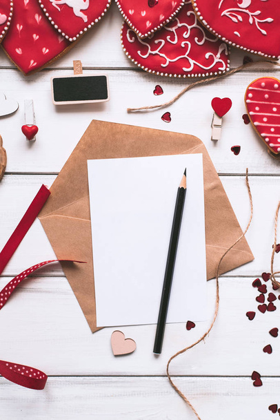 Festliche Komposition mit handgemachten rot glasierten Plätzchen, Brief, Papierstück und Bleistift auf Holzplanken Hintergrund für den Valentinstag. - Foto, Bild