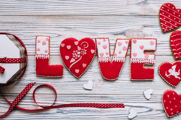 Святкова композиція з червоним глазурованим печивом з любов'ю, написом, стрічкою та коробкою на дерев'яних дошках фону для романтичного дня
. - Фото, зображення