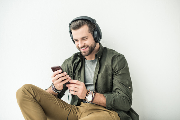 krásný usměvavý muž poslech hudby s smartphone izolované na bílém - Fotografie, Obrázek