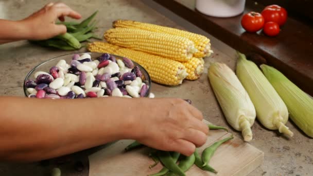 close up of female hands shelling fresh colorful beans into glass bowl near corn cobs - Footage, Video