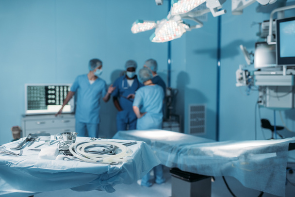 cuatro cirujanos multiétnicos en quirófano con herramientas en primer plano
 - Foto, Imagen