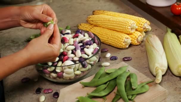 トウモロコシの穂軸の近くのガラスのボウルに新鮮なカラフルな豆を殻から取り出す女性の手のクローズ アップ - 映像、動画