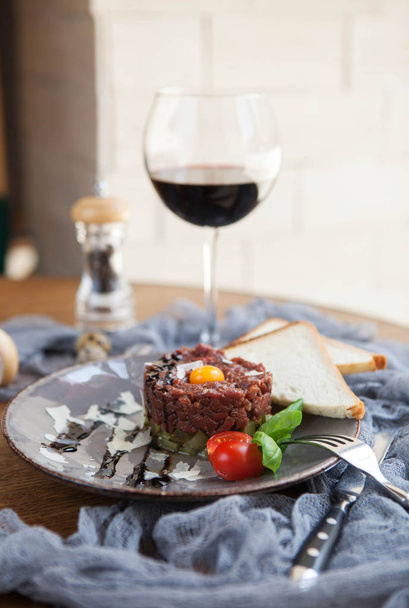 bela porção de tartare de carne com gema de ovo de codorna com duas fatias de pão e um copo de vinho em uma placa cinza
 - Foto, Imagem