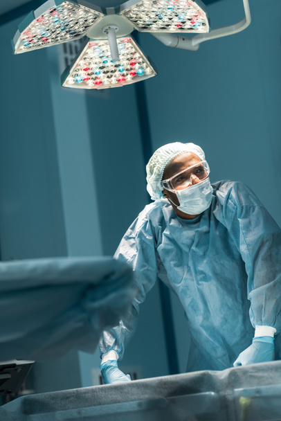 cansado afroamericano cirujano mirando hacia otro lado en el quirófano
 - Foto, imagen
