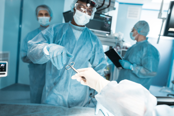 image recadrée de l'infirmière passant des ciseaux médicaux au chirurgien afro-américain
 - Photo, image