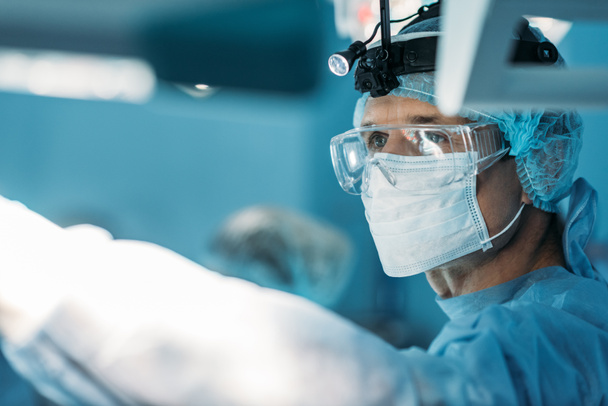 cirujano guapo en máscara médica y gafas mirando hacia otro lado
 - Foto, Imagen